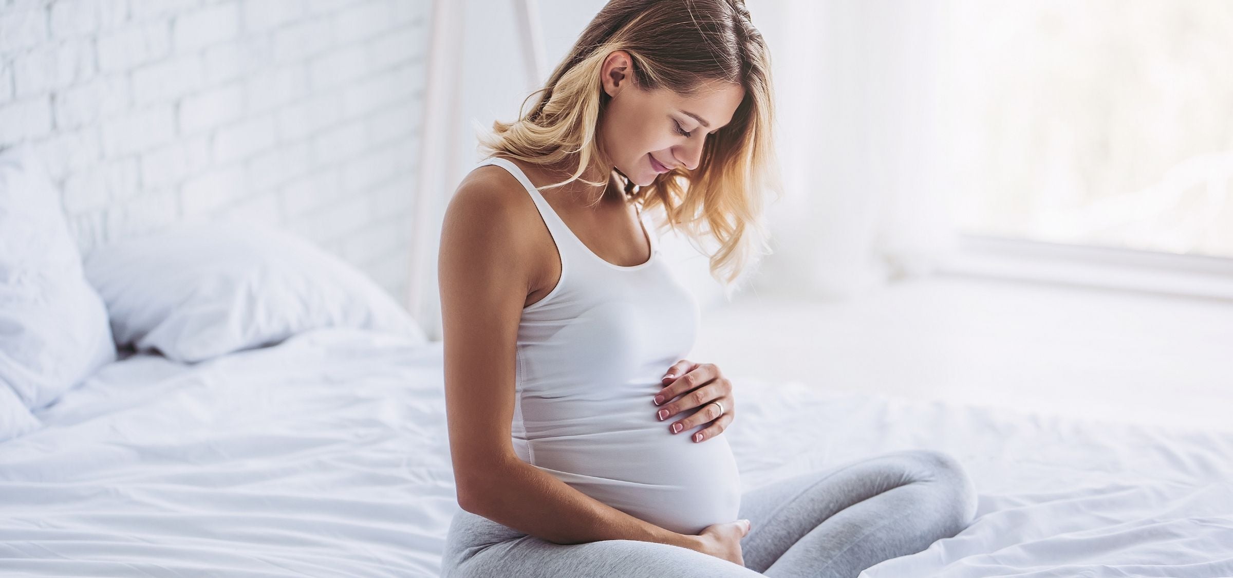 Frau mit Babybauch auf dem Bett: Hautpflege in der Schwangerschaft