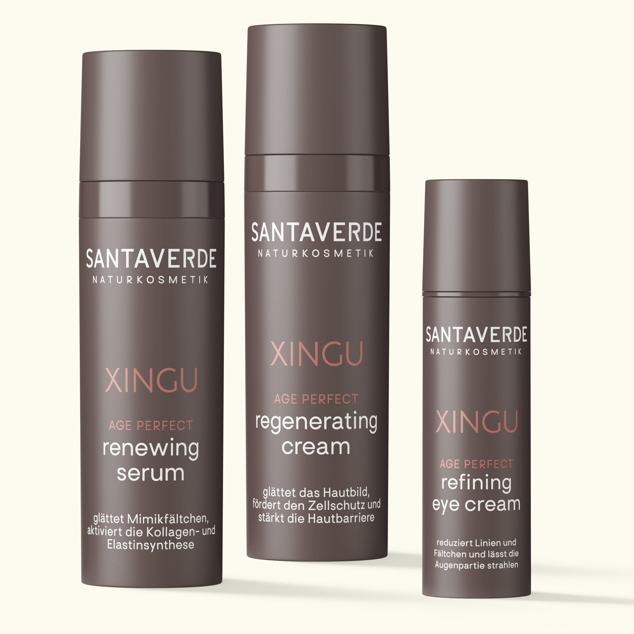 Drei Santaverde XINGU Age Perfect Produkte – renewing serum, regenerating cream und refining eye cream – in braunen Spenderflakons auf hellem Hintergrund nebeneinander stehend.