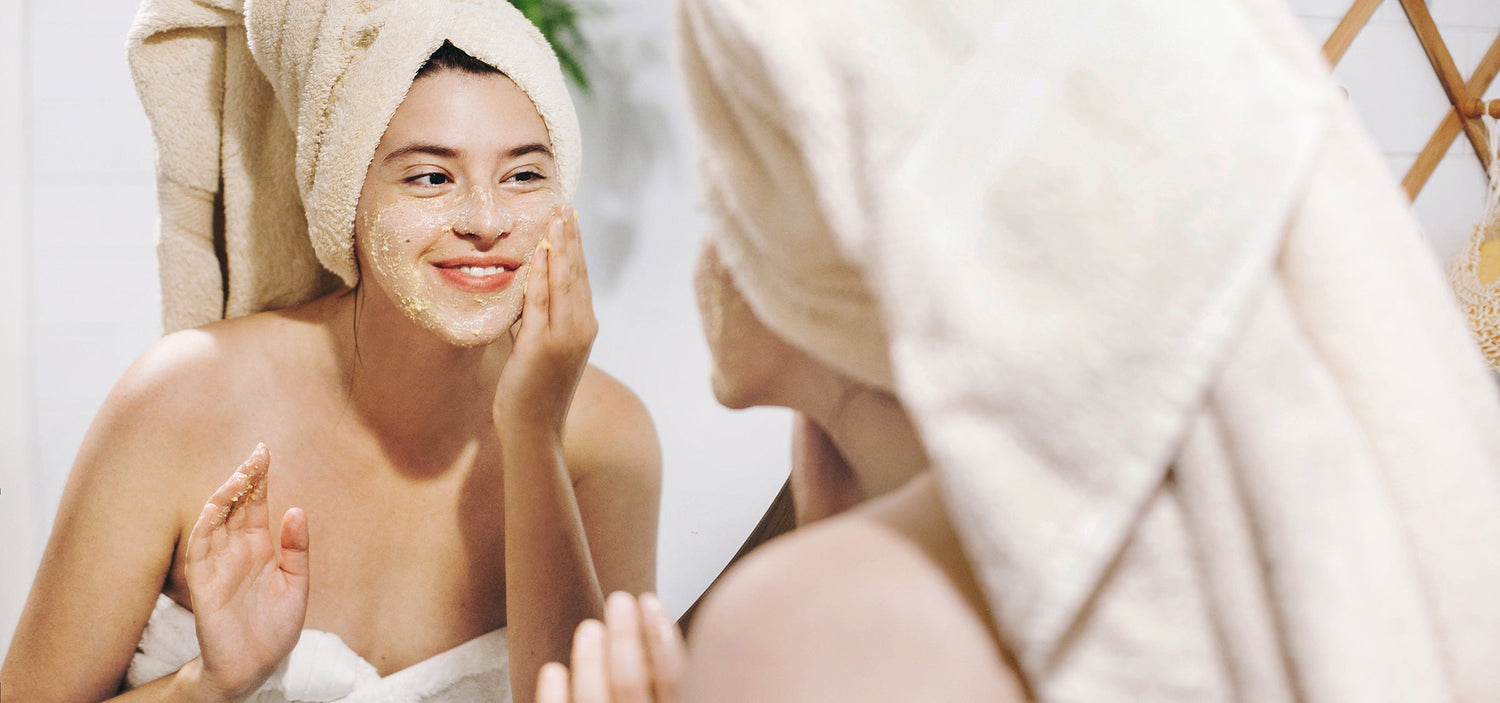 Frau schaut in Spiegel und peelt ihr Gesicht