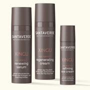 Drei Santaverde XINGU Age Perfect Produkte – renewing serum, regenerating cream und refining eye cream – in braunen Spenderflakons auf hellem Hintergrund nebeneinander stehend.